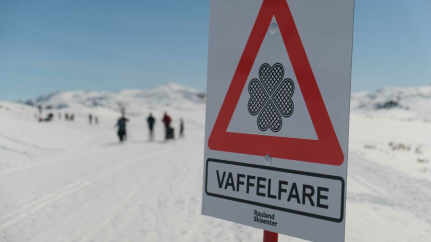 Skilt med Vaffelfare står ved snødekte løyper i Rauland Skisenter, Norge, med fjell i bakgrunnen.