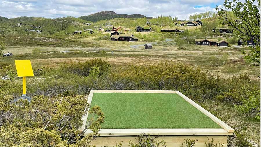 Utsikt over hyttefelt i norsk fjellandskap med en platting i forgrunnen.