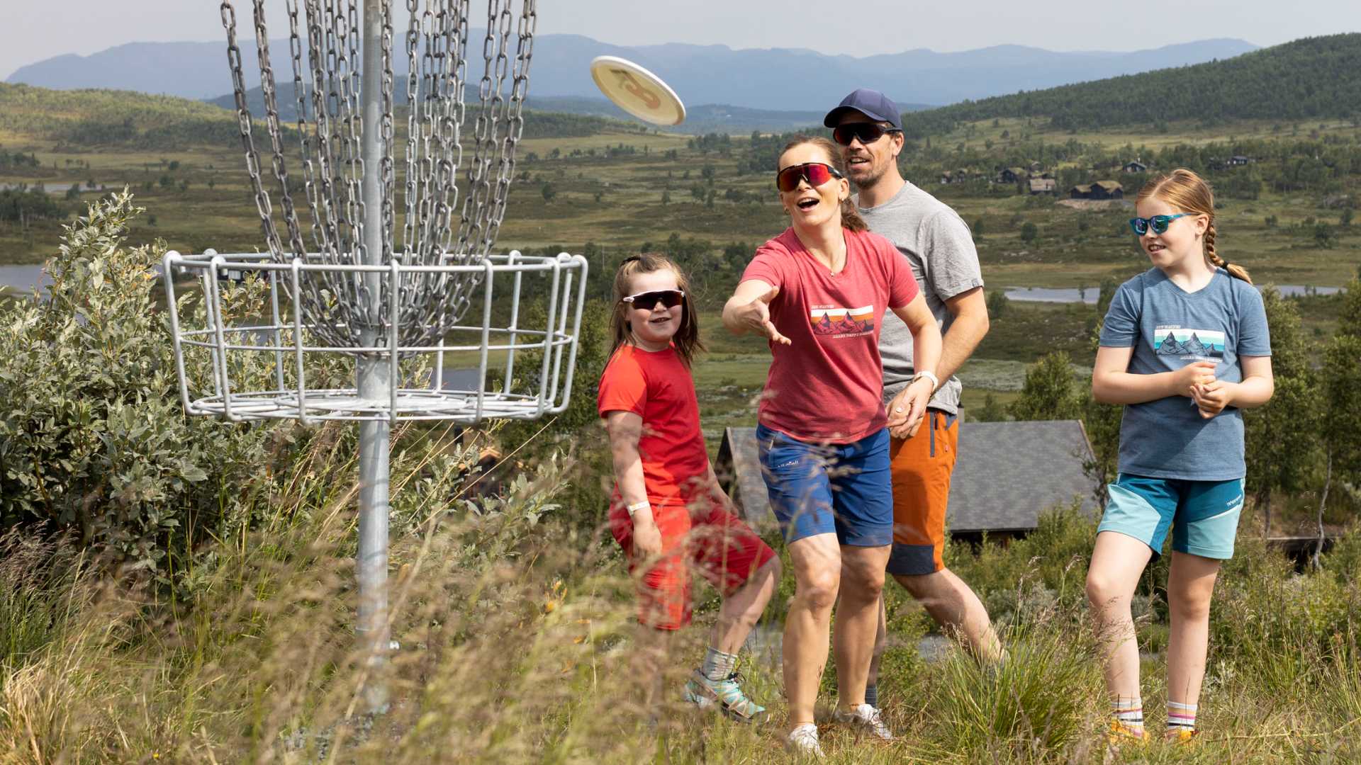 Familie nyter frisbee-golf i naturskjønne omgivelser på fjellet, med fokus på målkurv.