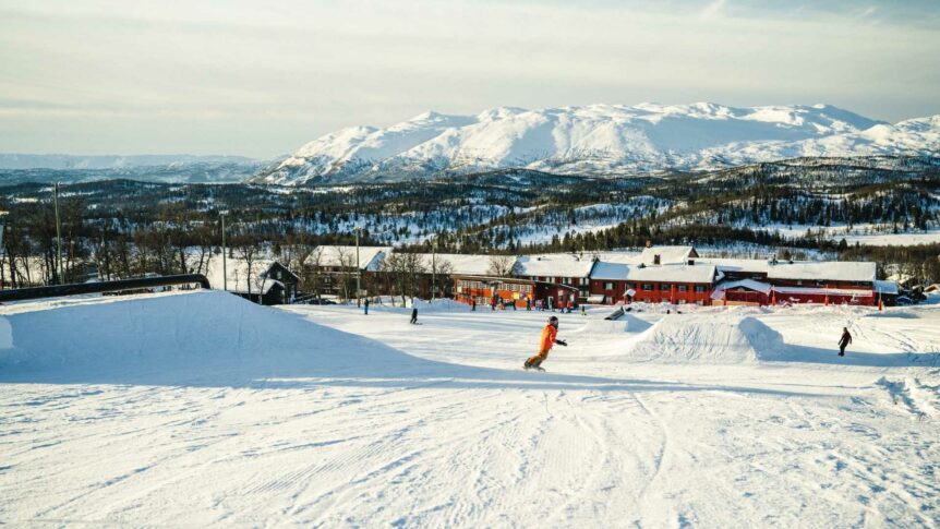 Snølandskap med en skibakke og personer som står på ski foran fjell i bakgrunnen, vinter i Norge.