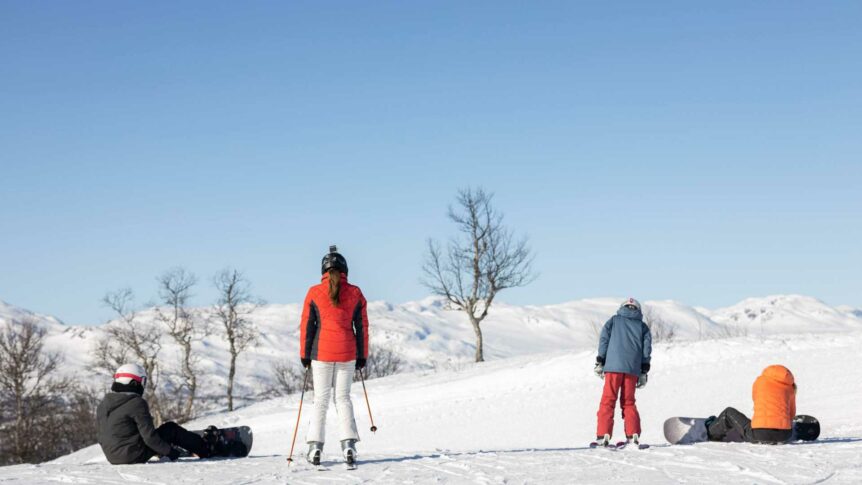 Personer på ski og snowboard på snødekte fjell med klar blå himmel i bakgrunnen. Vinteraktivitet i fjellet.