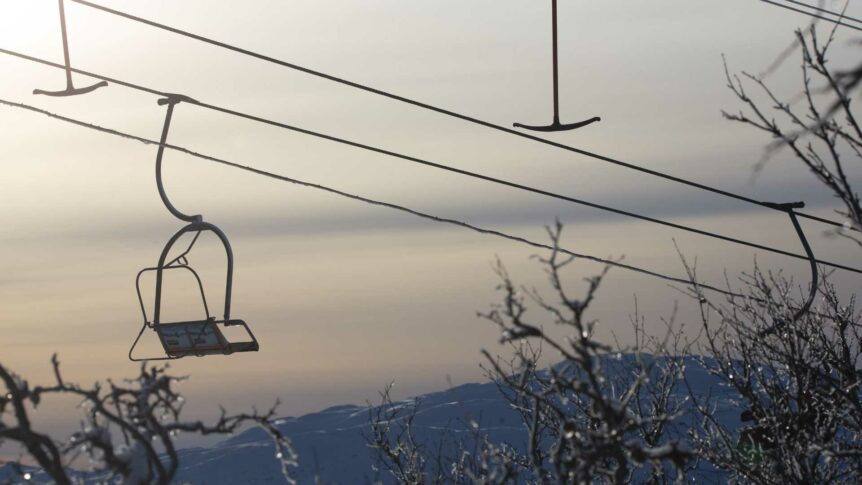 Skilift i solnedgang over en vinterfjellside med isdekte grener i forgrunnen.