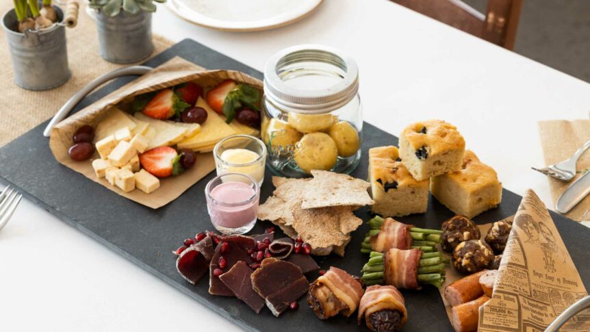 Et variert tapasbord med oster, frukt, grønnsaker, poteter, og kjøttretter på svart skiferbrett.