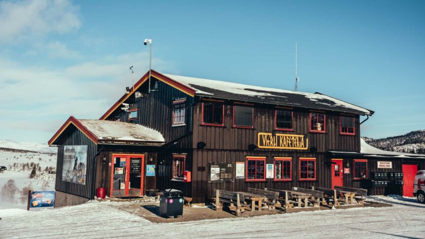 Uavhengig kafé på fjellet med snødekt landskap og klar blå himmel i bakgrunnen.