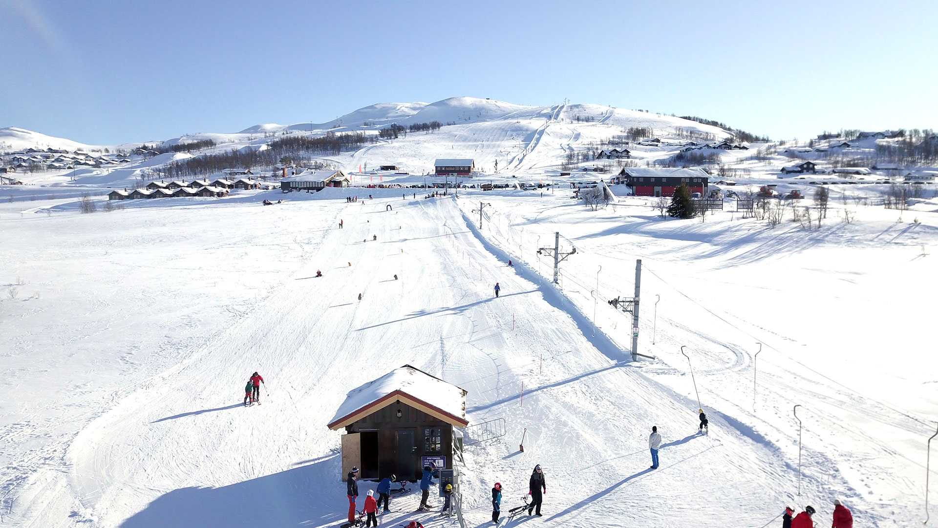 Snødekt fjellandskap med skianlegg, skiheis og hytter under klar blå himmel. Vinteraktiviteter i Norge.