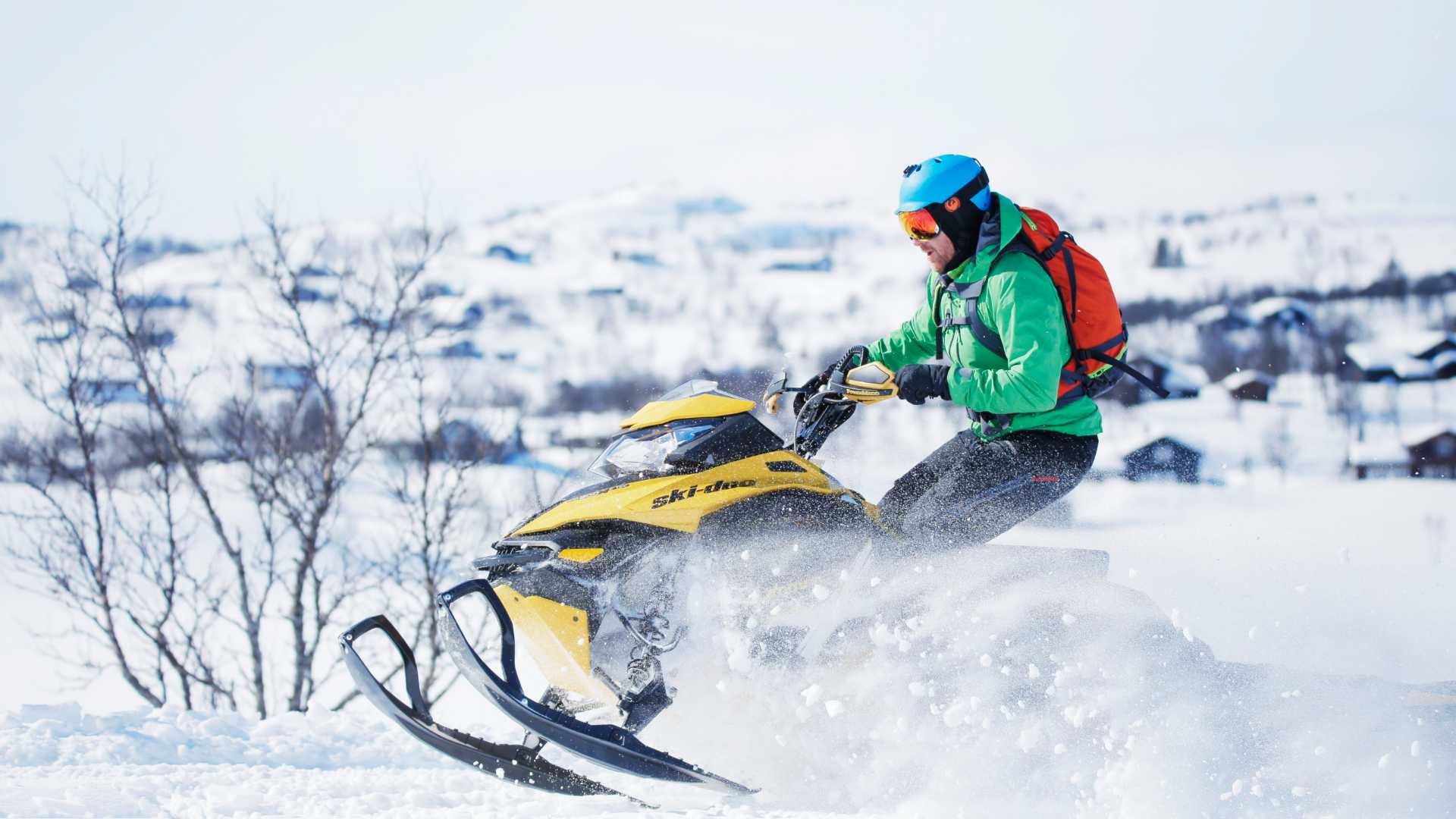 En person på snøscooter kjører gjennom snølandskap iført grønn jakke og blå hjelm, vinteraktiviteter i Norge.