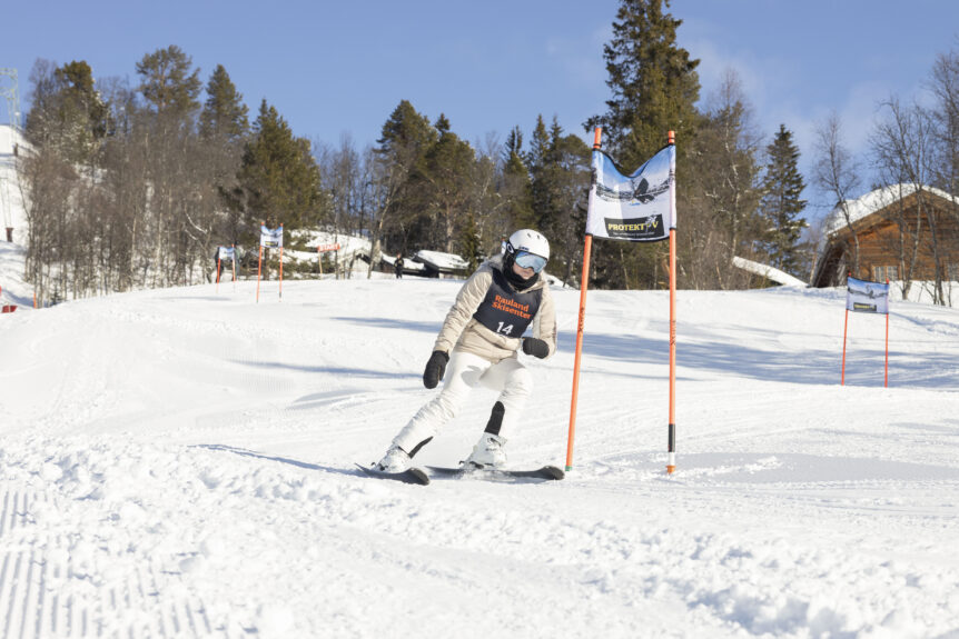 Skientusiast i hvit drakt suser nedover bakkens snødekte løyper under en skyfri himmel i Rauland Skisenter.