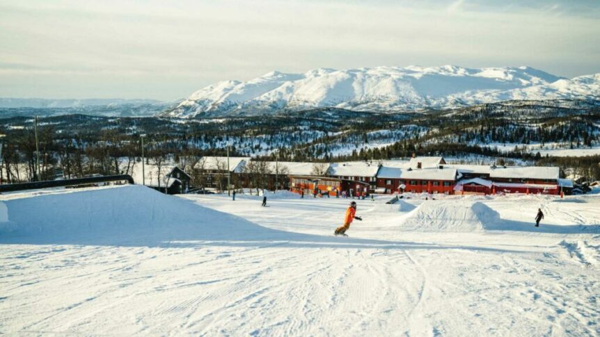 Person snowboarder i vinterlandskap med fjell og hytter i bakgrunnen i Norge. Perfekt for vintersport.