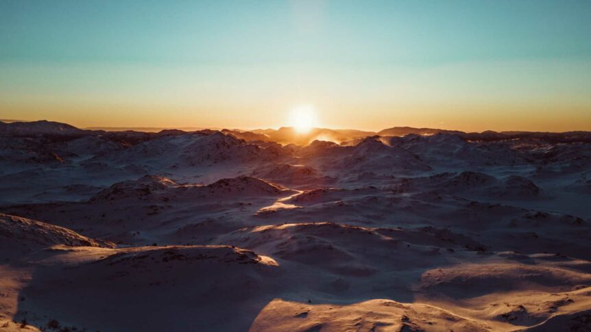 Solnedgang over snødekte fjell, vakkert lys i horisonten. Vinterlandskap med rolig atmosfære.