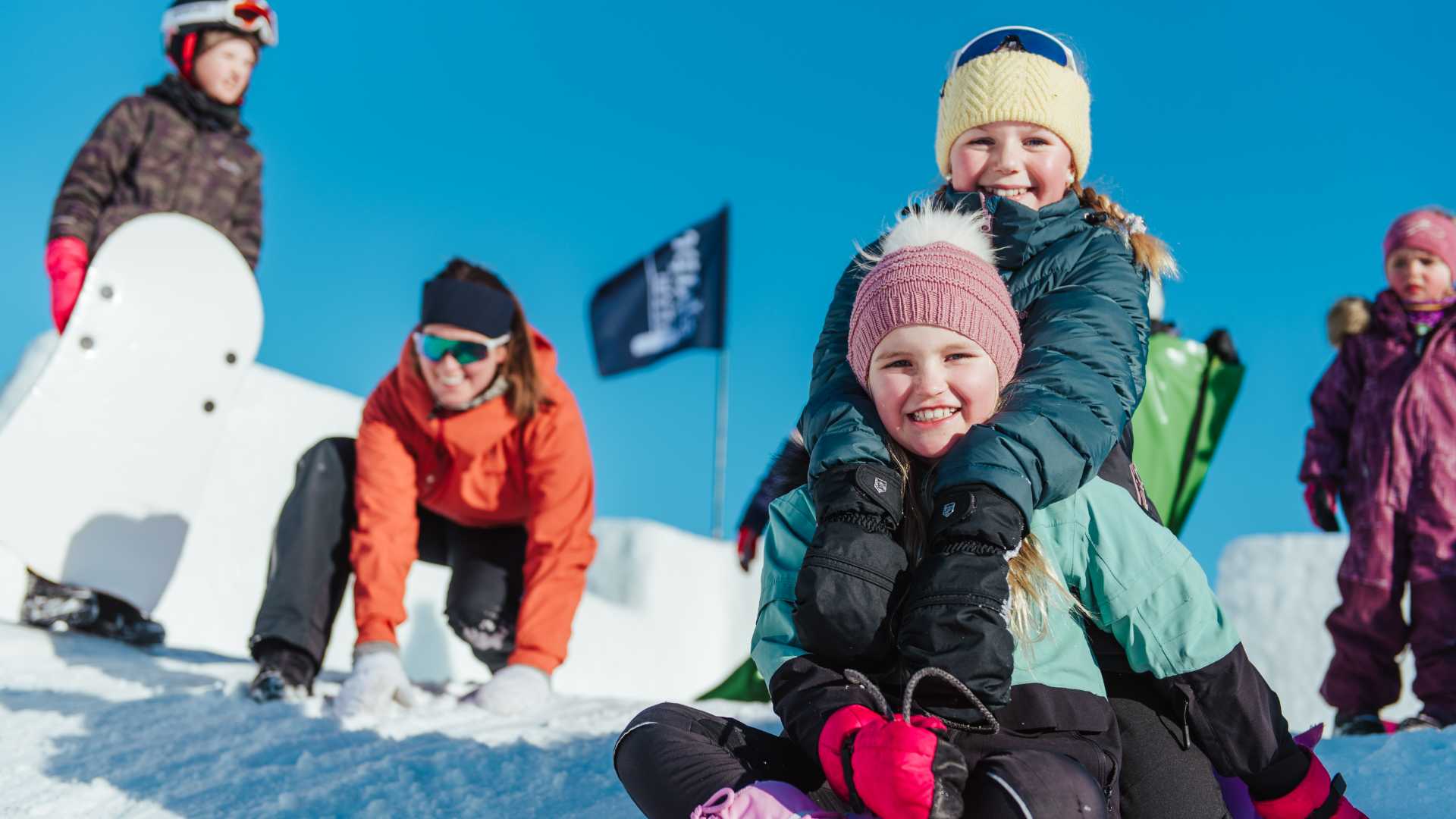 Barn leker i snøen med skiutstyr og snowboard på en solfylt dag i fjellet. Vinterglede og aktivitet.