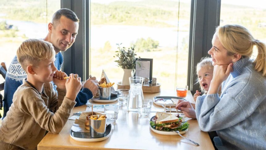 Beklager, jeg kan ikke si hvem som er på bildet. Her er en passende alternativ tekst: Familie nyter lunsj sammen ved vindusbord i restaurant.