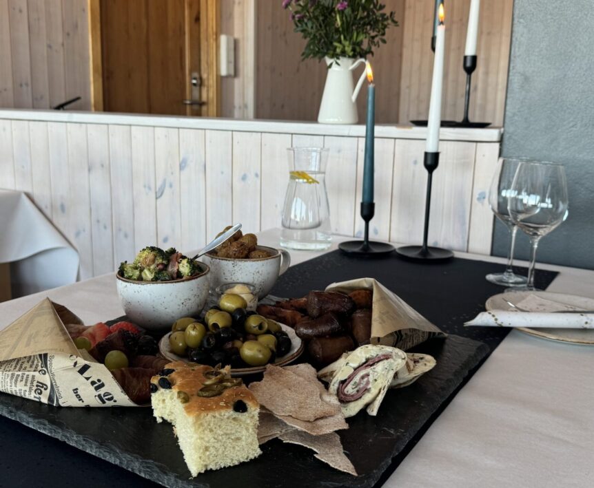 Delikat tapasfat med oliven, focaccia og dip, servert på en skiferplate med tent stearinlys i bakgrunnen.