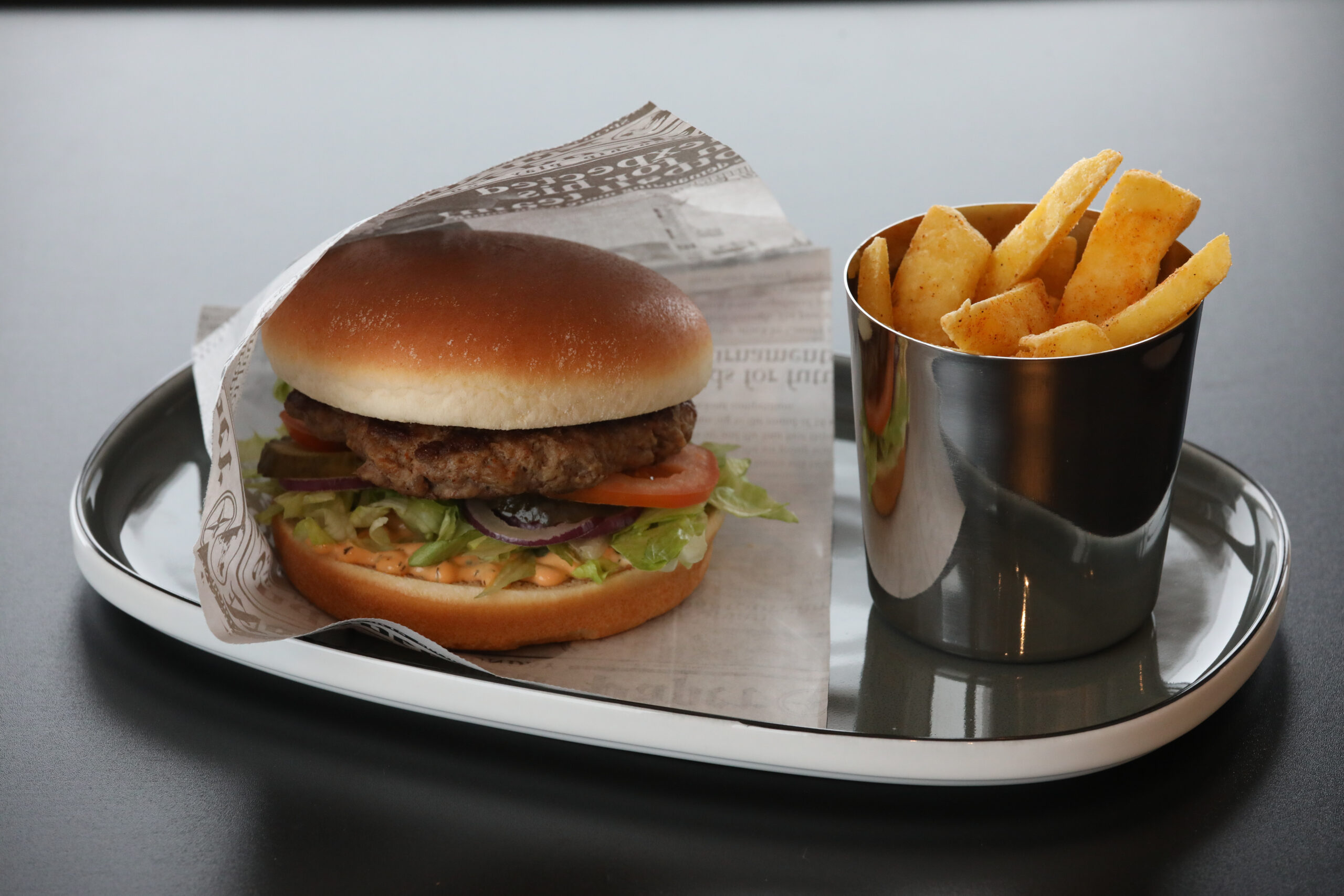 Burger med salat, tomat og løk, servert med sprø pommes frites i metallkopp på fat.