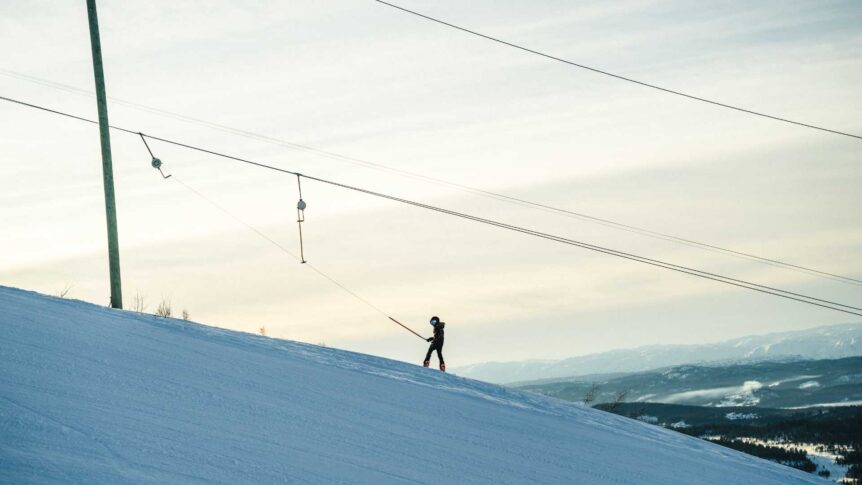 Person som bruker skitrekk på snødekt bakke med fjell i bakgrunnen.