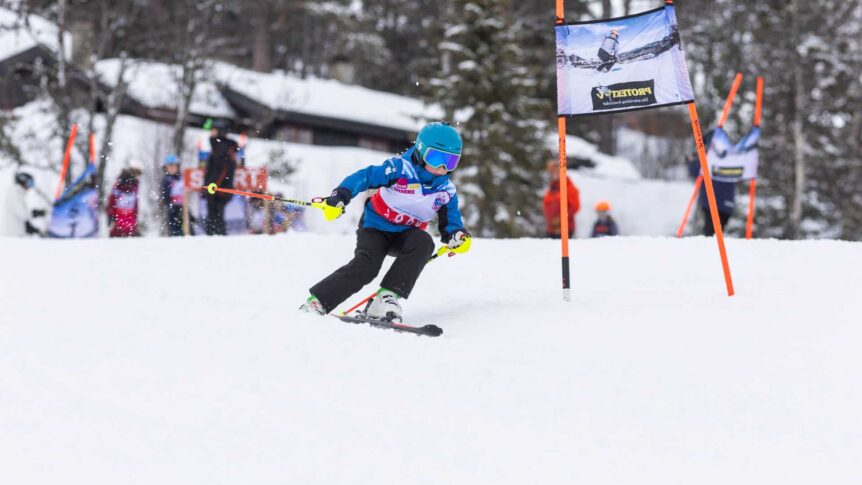 Barn på ski konkurrerer i slalåm med hjelm og briller. Snødekt bakgrunn med skiport. Vinterlandskap.