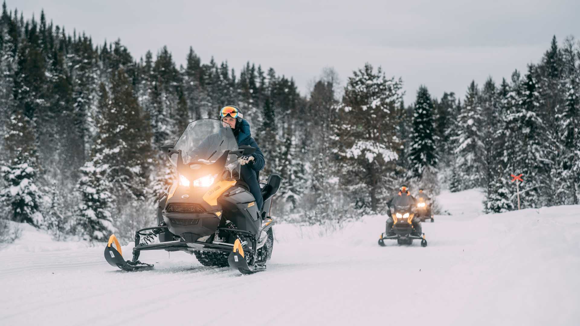 Person kjører snøscooter gjennom en snødekket skog med vinterlandskap i bakgrunnen.