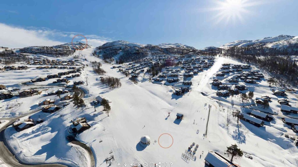 Panoramautsikt over snøkledd skianlegg med fjellhytter og klarlå himmel i Norge.