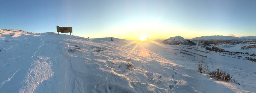Soloppgang over snødekket fjellandskap med blå himmel. Perfekt for vinteraktiviteter og spektakulær natur.