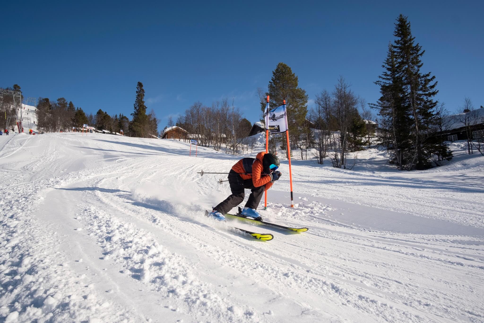 Person som står på ski i høy fart ned en snødekt bakke under klar blå himmel.