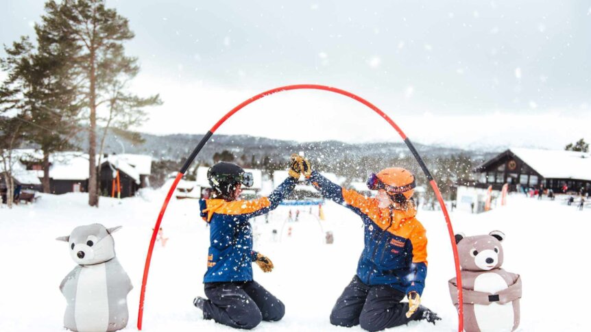 To personer i vintersportsutstyr feirer i snøen under en lekeaktivitet med snøkaniner.