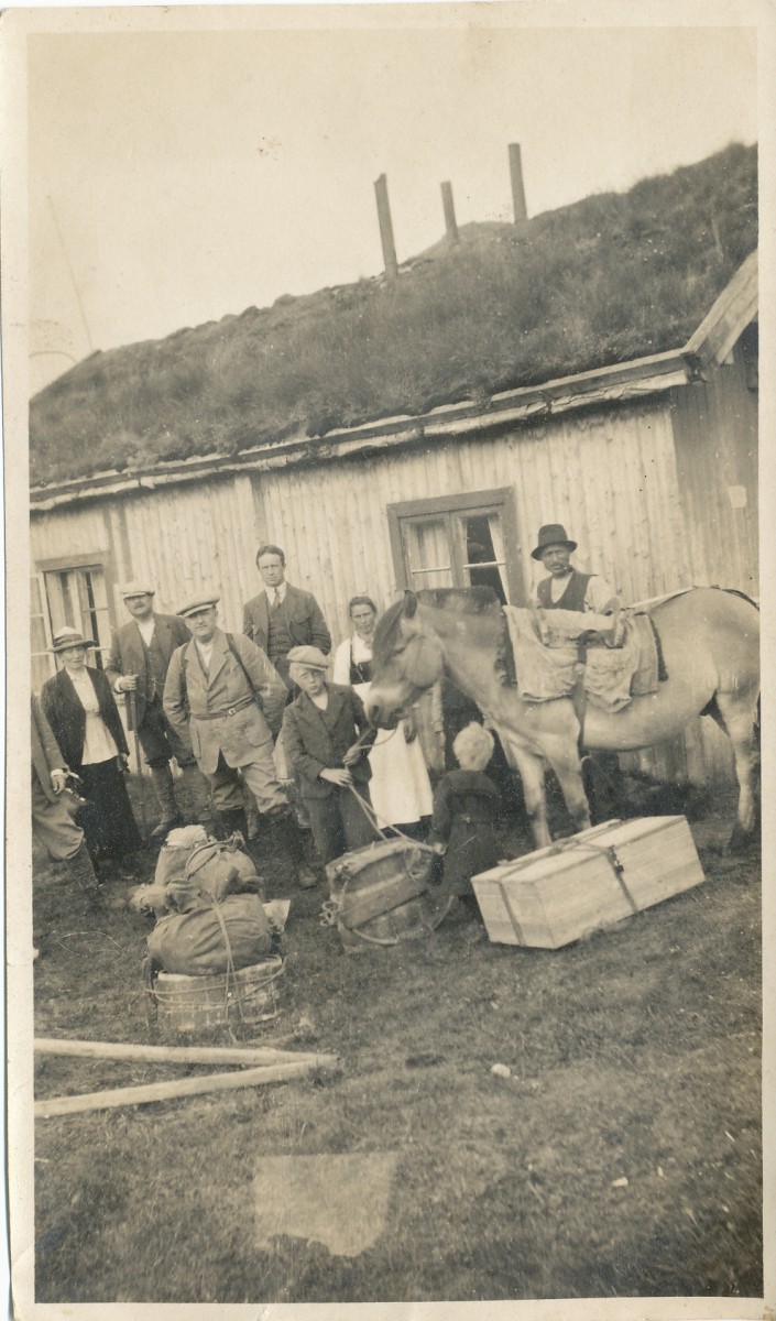 Gruppe foran hus, hest med last og kofferter. Vintage foto, tradisjonell norsk gård. Historisk reisebilde.