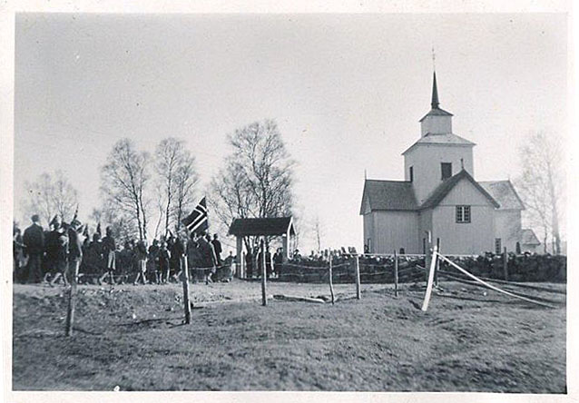 Sort-hvitt bilde av en kirke med en gruppe mennesker som holder et norsk flagg.