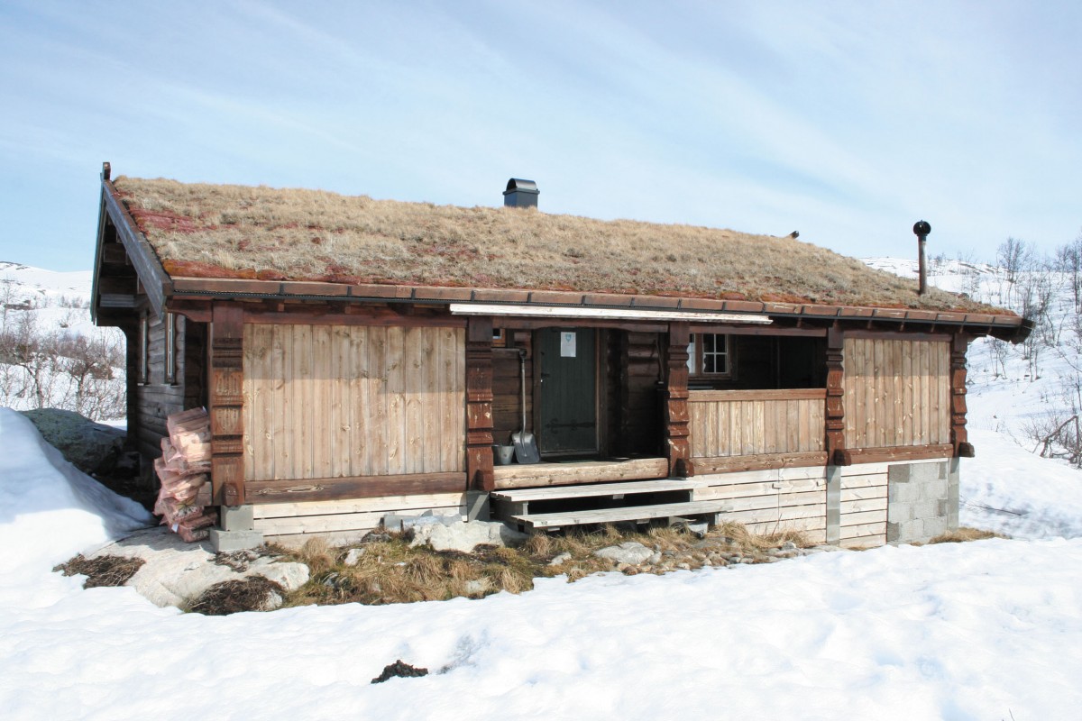 Norsk hytte med torvtak i snølandskap, tradisjonell arkitektur i fjellomgivelser.