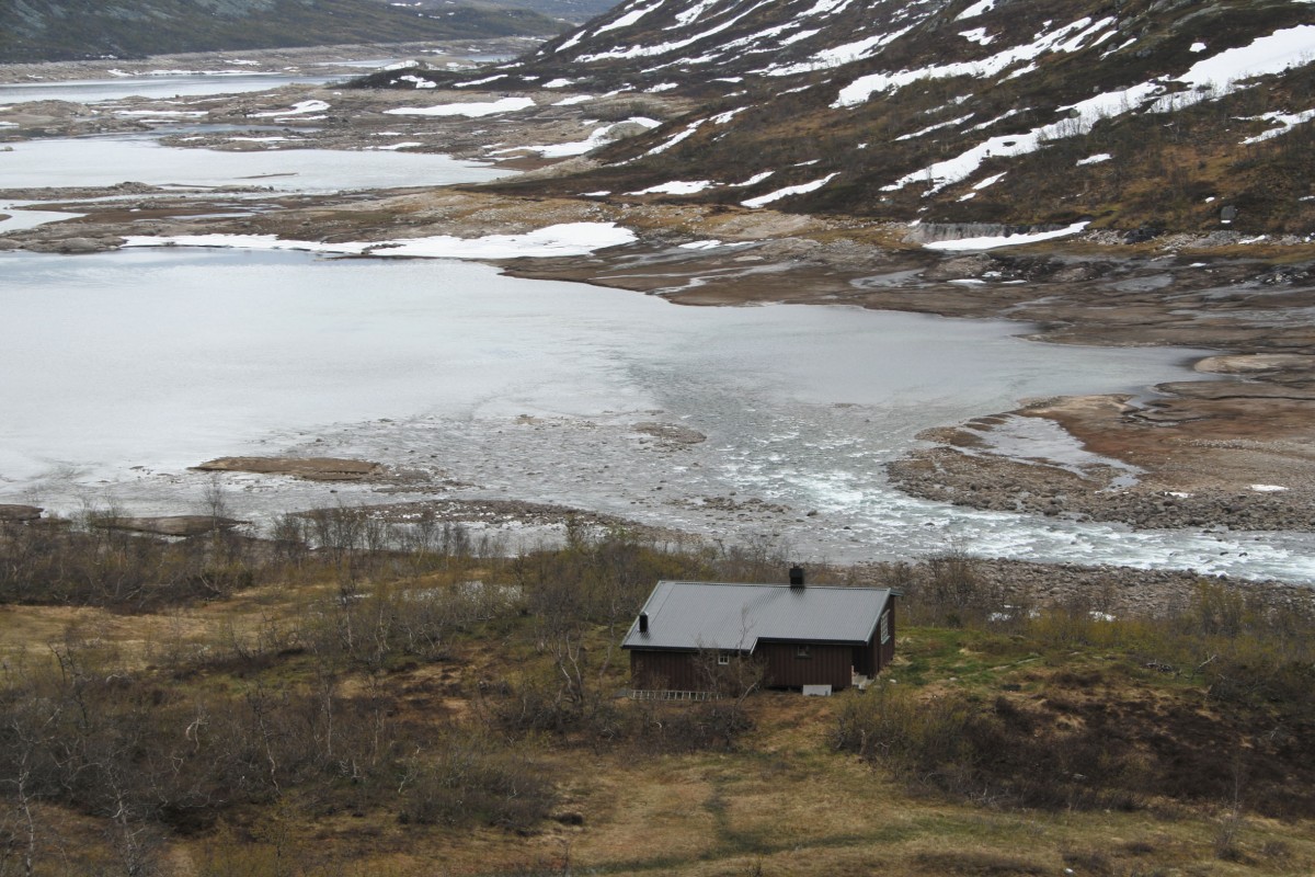 Hytte ved isdekket innsjø og fjell i Norge. Vinterfarger og snødekte fjell.