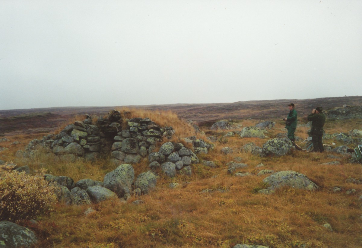 To personer ved en steinformasjon på et høstlig landskap med lav vegetasjon og overskyet himmel.