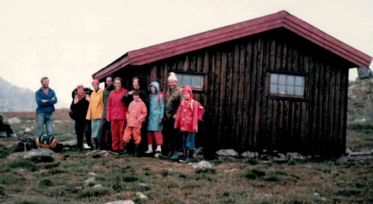 Gruppe i fargerike regnjakker foran hytte i norsk natur.