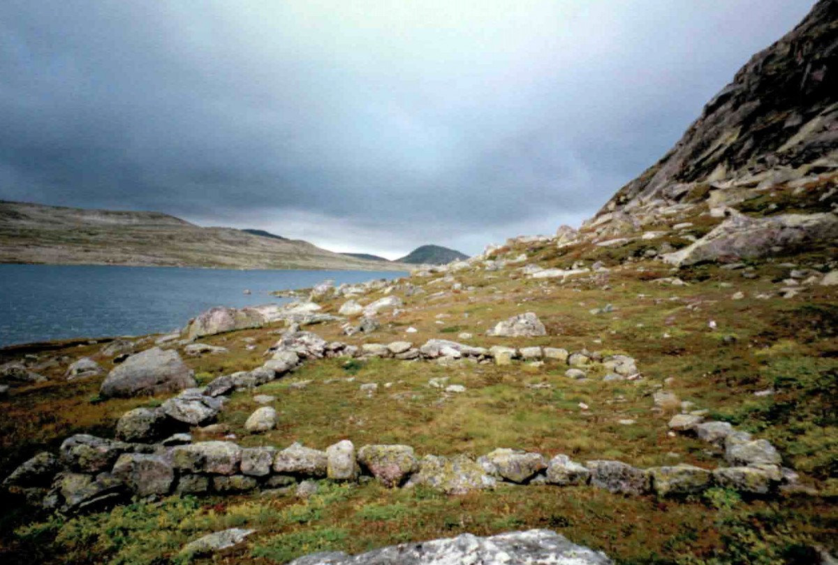 Forlatte steinmurer ved en innsjø i et norsk fjellandskap under en overskyet himmel.