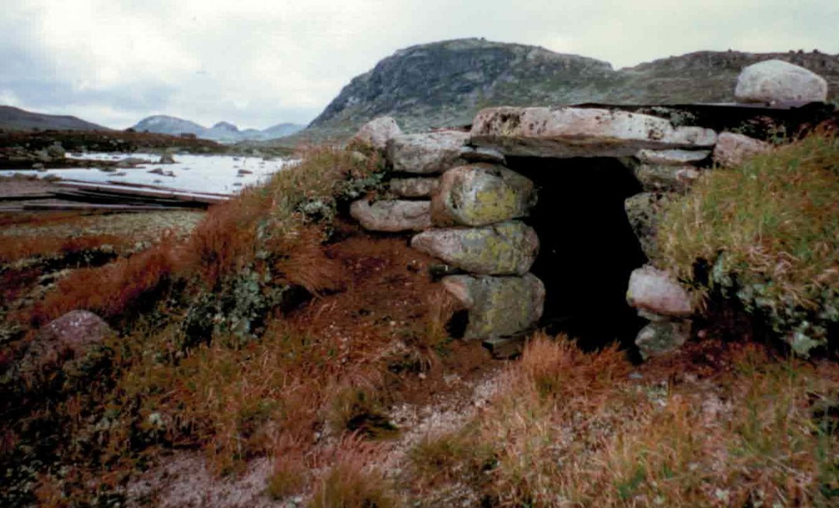Steinhytte i fjellandskap med bakgrunn av snødekte topper. Naturlig, historisk struktur i norsk natur.