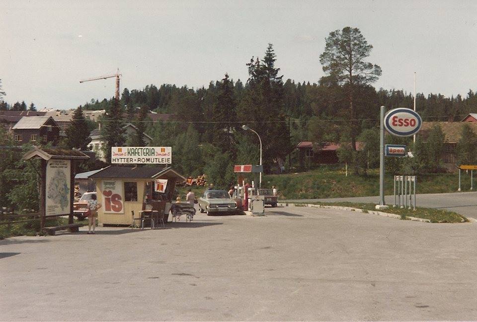 Esso bensinstasjon og kafeteria i landlig område, Norge, med biler og skog i bakgrunnen.