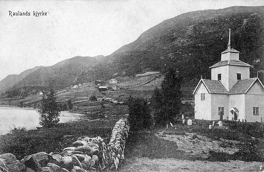 Sort-hvitt bilde av Rauland kirke i fjellandskap. Kirke, fjell og vann vises i bakgrunnen.
