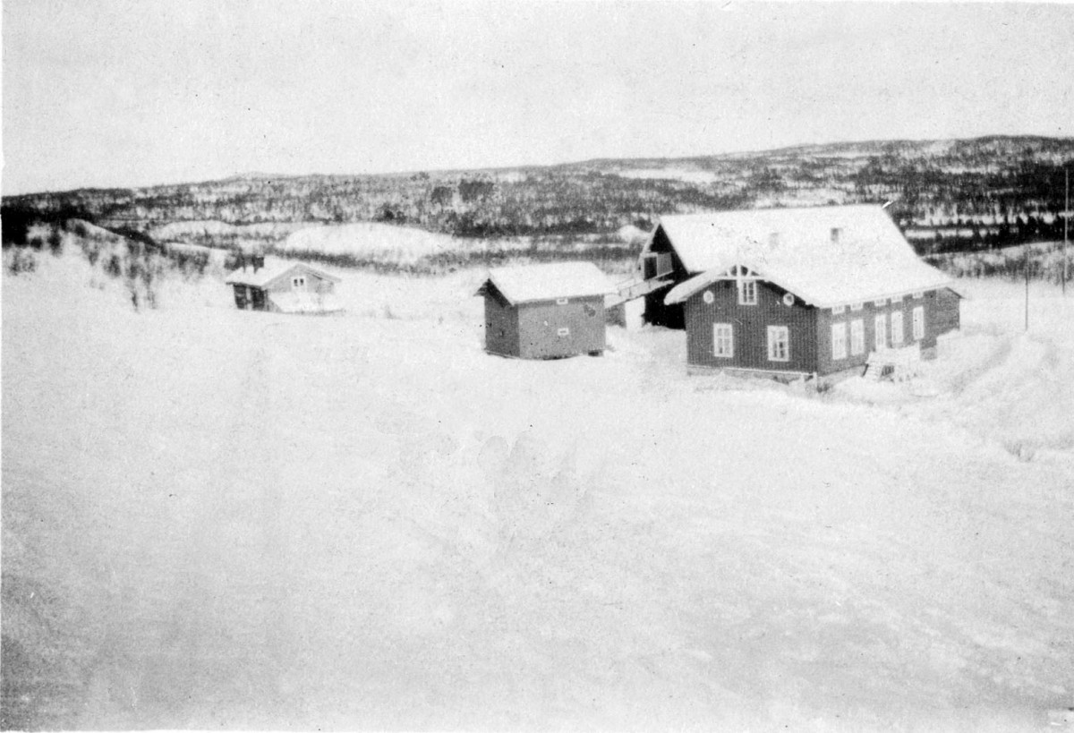 Snødekt gårdstun i Norge med tradisjonelle trehus og vinterlandskap i bakgrunnen.