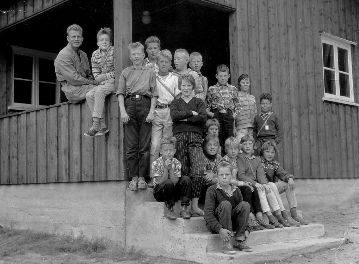 Svart-hvitt bilde av en gruppe barn foran en trebygning, cirka 1950-tallet.