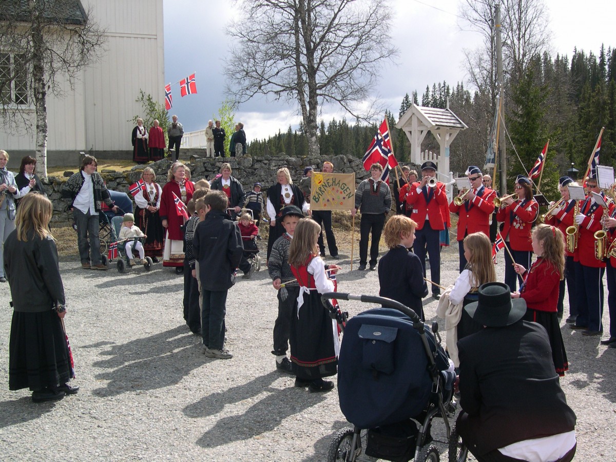 17. mai-feiring i Norge: folk i tradisjonelle klær, korps og norske flagg ved en kirke.