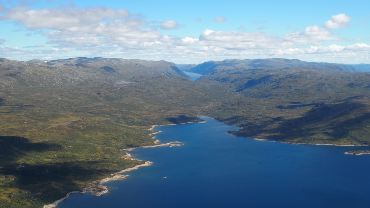 Luftfoto av innsjø omgitt av fjellandskap under en klar himmel i Norge.