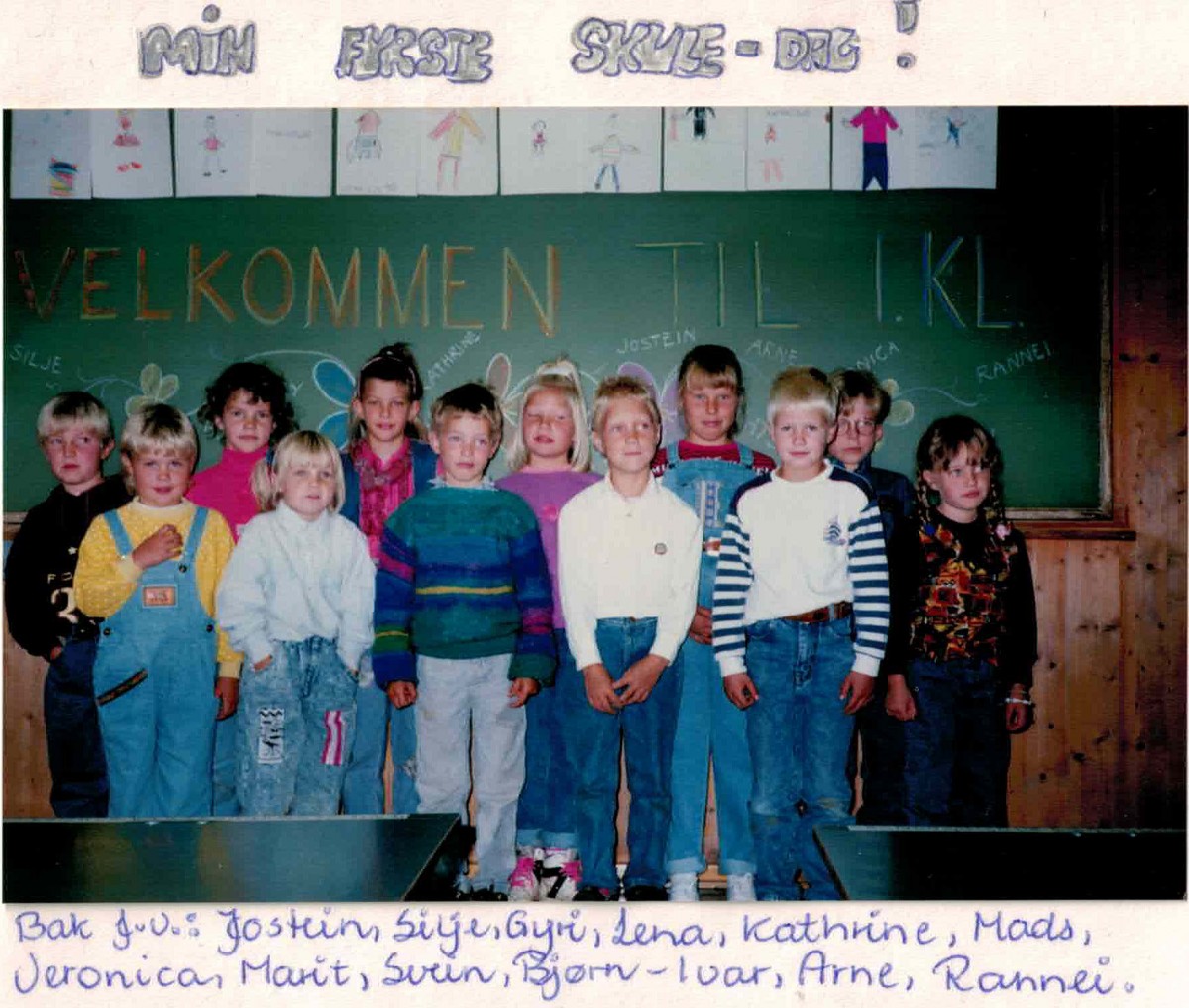 En gruppe barn poserer foran en tavle med teksten Velkommen til 1. kl. i et klasserom.