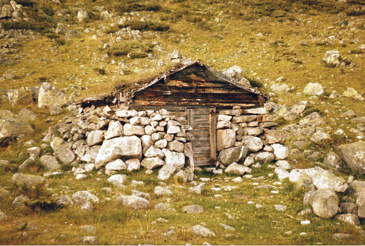 Gammel steinhytte i norsk fjellandskap, omgitt av gress og steiner. Rustikk arkitektur i naturen.