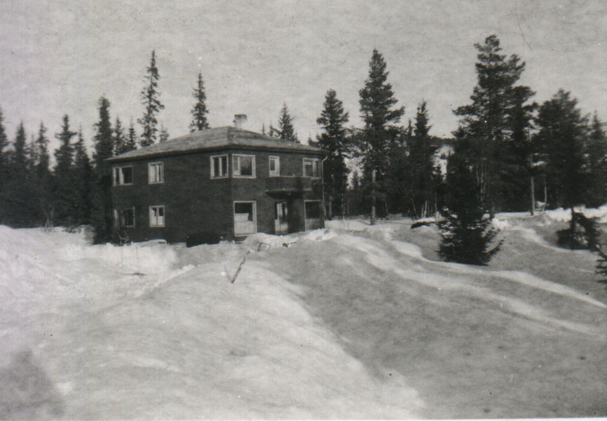 Et gammelt hus om vinteren omgitt av snødekte trær i et skogsområde.