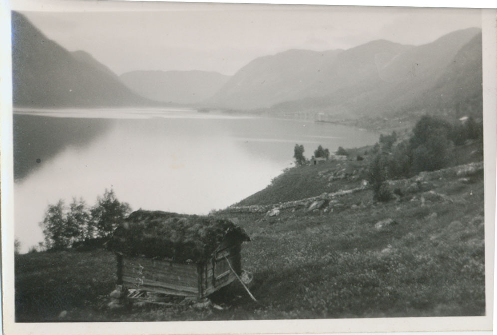 Gammelt naust ved stille fjord omgitt av majestetiske fjell i Sogn, Norge.