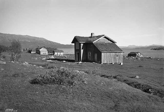 Gammelt trehus i norsk landskap med fjell og innsjø i bakgrunnen, gir en følelse av ro og natur.