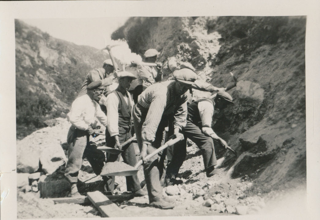 Arbeidere graver i fjellet med spader, tidlig 1900-tall, svart-hvitt bilde av tungt arbeid i fjellandskap.