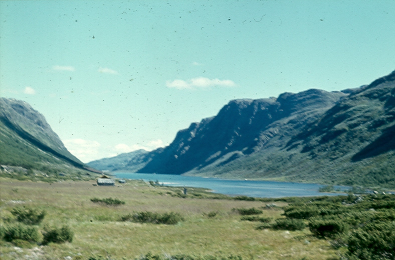 Naturskjønn dal med innsjø og fjell i bakgrunnen under blå himmel. Norsk landskap om sommeren.