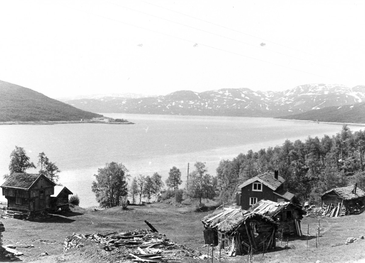 Svart-hvitt landskap med trehus, innsjø og fjell i Nord-Norge. Historisk fjordutsikt med tradisjonelle bygninger.