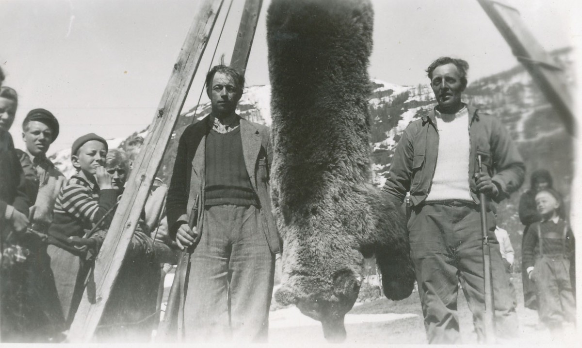 Jaktlag med fellet bjørn i norsk fjellandskap, svart-hvitt bilde fra tidlig 1900-tall.