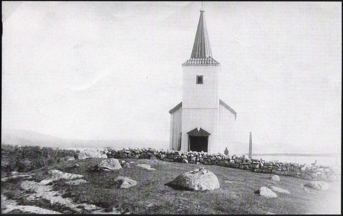 Gammel kirke med spir i steinlagt landskap, historisk bilde.