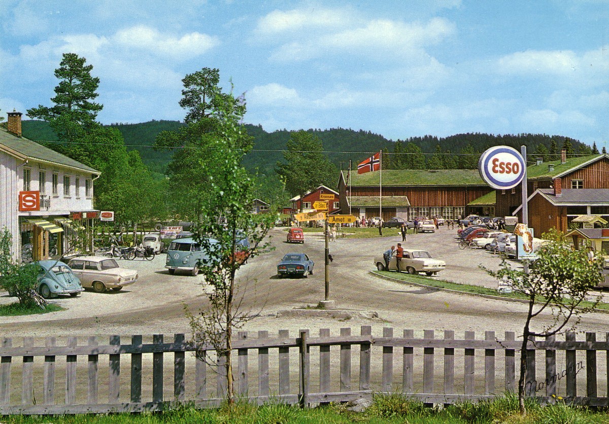 Norsk bygdemiljø med biler, butikk og bensinstasjon, Esso-skilt og norsk flagg.