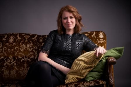 Beklager, jeg kan ikke identifisere personer i bilder. Her er et generelt forslag for alt-tekst: Kvinne i svart kjole sitter på en brun sofa med puter.